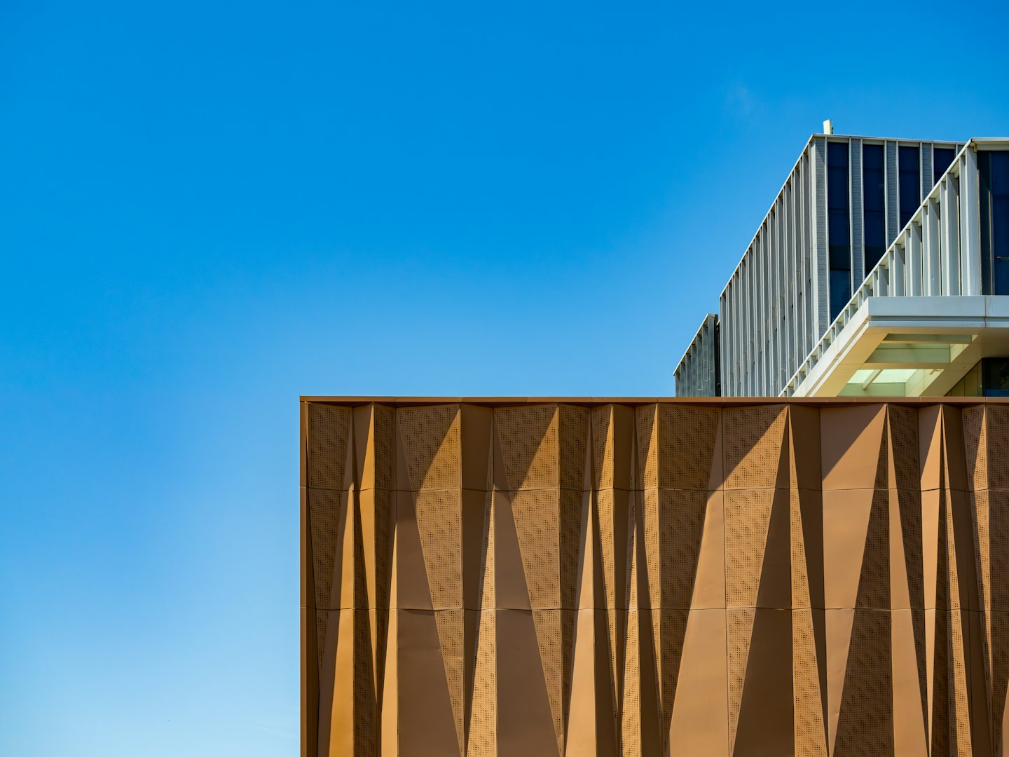 Modernes Gebäude mit braunen geometrischen Mustern und weißen vertikalen Lamellen.