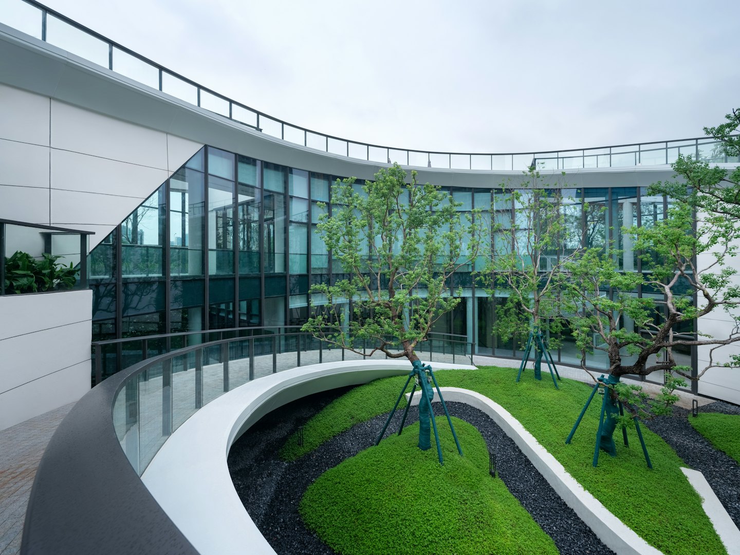Modernes Gebäude mit Glaswänden blickt auf einen begrünten Gartenhof.