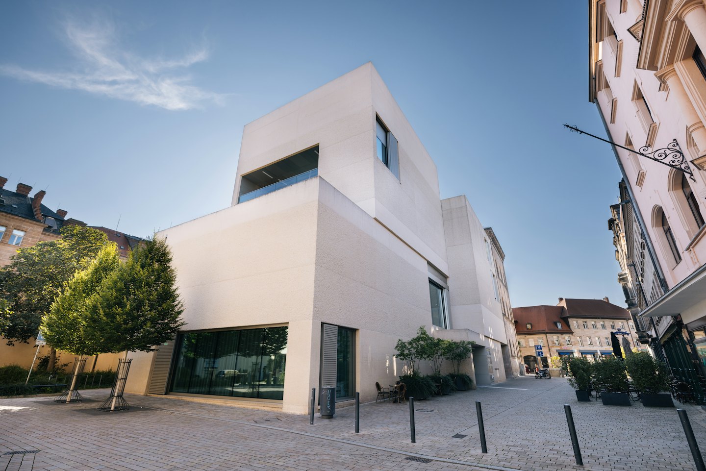 Modernes Betongebäude mit Glasfenstern an einer kopfsteingepflasterten Straße.
